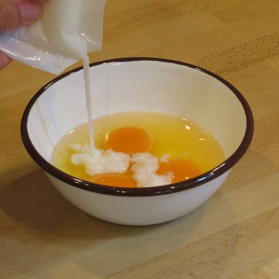3個の卵が割られた器の中に、袋から白い液体を流し込んでいる様子。