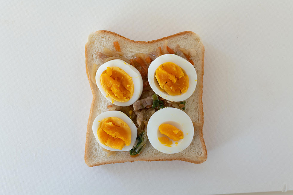 お弁当用の惣菜2種をのせた食パンの上に、ゆで卵をバランスよく重ねる。