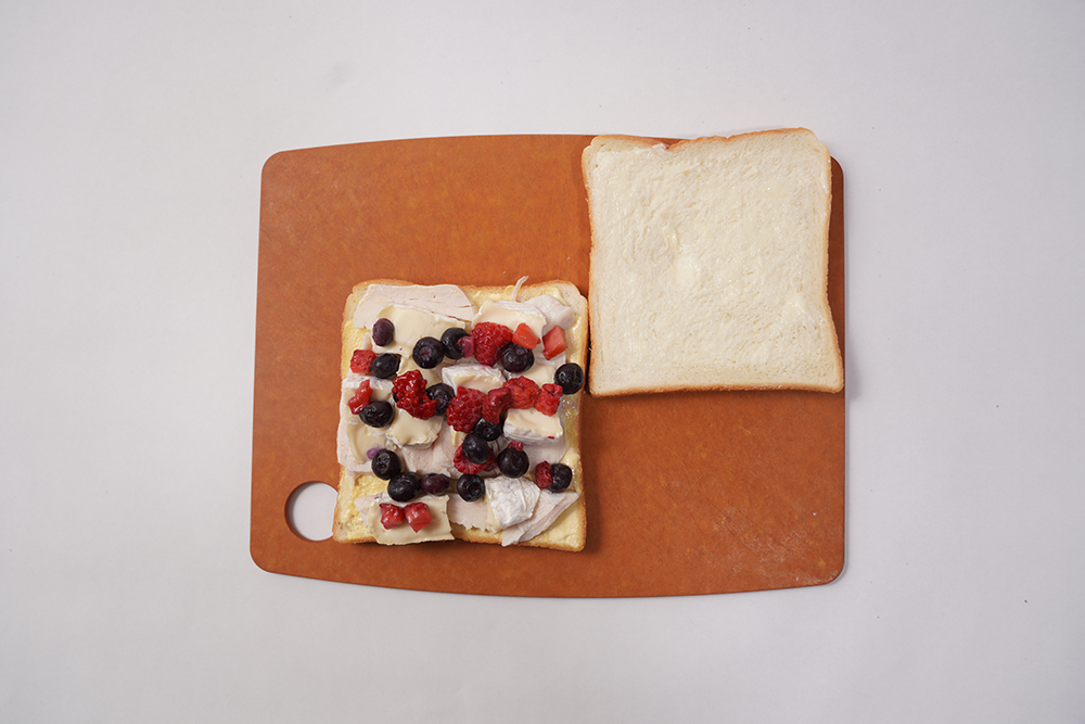 マヨネーズとマスタードを塗ったパンの上に、サラダチキン、カマンベールチーズ、冷凍ベリーをはみ出さないように重ねる。